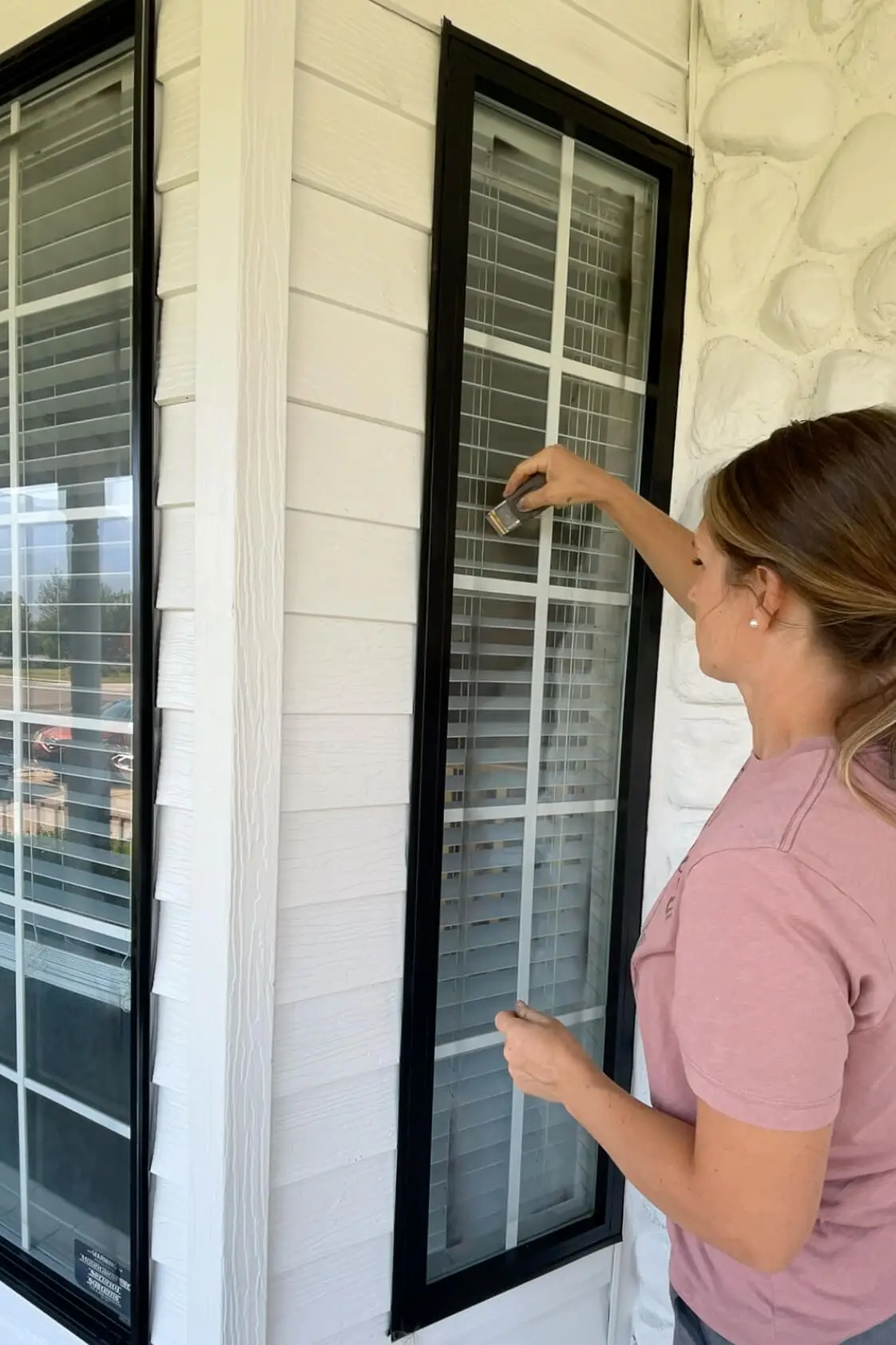 Woman using a razor blade to remove overspray from a freshly spray painted window frame.